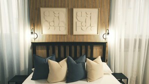 Una cama bien tendida con cabecera de madera, flanqueada por dos lámparas fijadas a la pared.