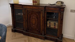 Un aparador de madera con puertas de cristal, una lámpara y cuadros en la pared.