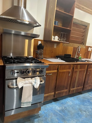 Una cocina con estufa de acero inoxidable, horno y un armario de madera con un estante sobre el lavamanos.