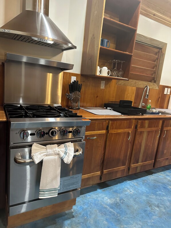 A kitchen with a stainless steel stove, oven, and a wooden cabinet with a shelf above the sink.