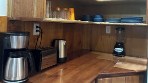 Cocina compacta con armarios de madera, cafetera, tostadora, hervidor y licuadora sobre la encimera.