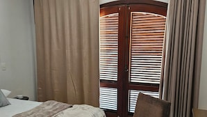 Ein Schlafzimmer mit einem Bett, einem Sessel, Holzboden und einem Fenster mit Jalousien.