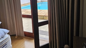 Eine geöffnete Tür führt zu einem Poolbereich mit Blick auf eine Palme und eine geflieste Terrasse.