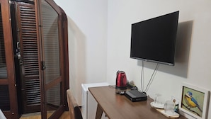 Ein Zimmer mit Schreibtisch aus Holz, einem an der Wand befestigten Fernseher, einem roten Wasserkocher und einem Bilderrahmen mit einem Vogelbild.