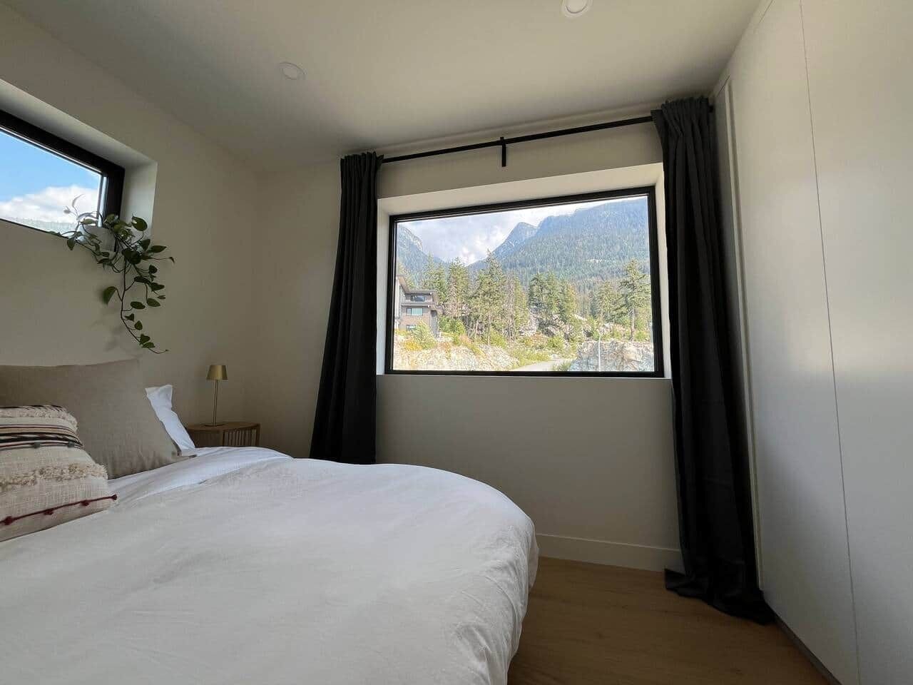 Une chambre avec un grand lit, une fenêtre donnant sur la montagne, une table de chevet avec une lampe et une plante accrochée au mur.