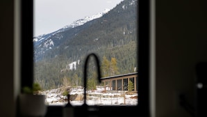 Vista per la finestra d'un paisatge de muntanya amb un edifici modern i una muntanya coberta de neu.