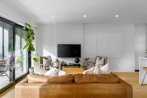 A modern living room with a leather sofa, a flat-screen TV, and a large window. - Spacious 2BR Retreat | Scenic Views | Modern & New (Whistler)