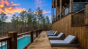 A wooden deck with lounge chairs overlooking a pool and forest. - Wild & Free | Luxury 7BR Cabin w/ Heated Pool, Pickleball Court, Game Loft & Multiple King Suites (Broken Bow)