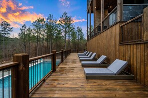 A wooden deck with lounge chairs overlooking a pool and forest. - Wild & Free | Luxury 7BR Cabin w/ Heated Pool, Pickleball Court, Game Loft & Multiple King Suites (Broken Bow)