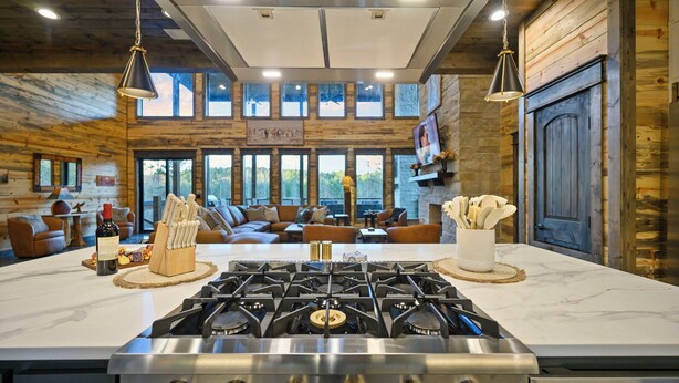 A modern kitchen with a gas stove, wooden walls, and a large window overlooking a forest. - Wild & Free | Luxury 7BR Cabin w/ Heated Pool, Pickleball Court, Game Loft & Multiple King Suites (Broken Bow)