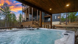 A hot tub with wooden deck and stairs leading to a building with a balcony. - Wild & Free | Luxury 7BR Cabin w/ Heated Pool, Pickleball Court, Game Loft & Multiple King Suites (Broken Bow)