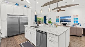 Une cuisine moderne dotée d’appareils électroménagers en acier inoxydable, d’un îlot central, de luminaires suspendus et d’un ventilateur de plafond.