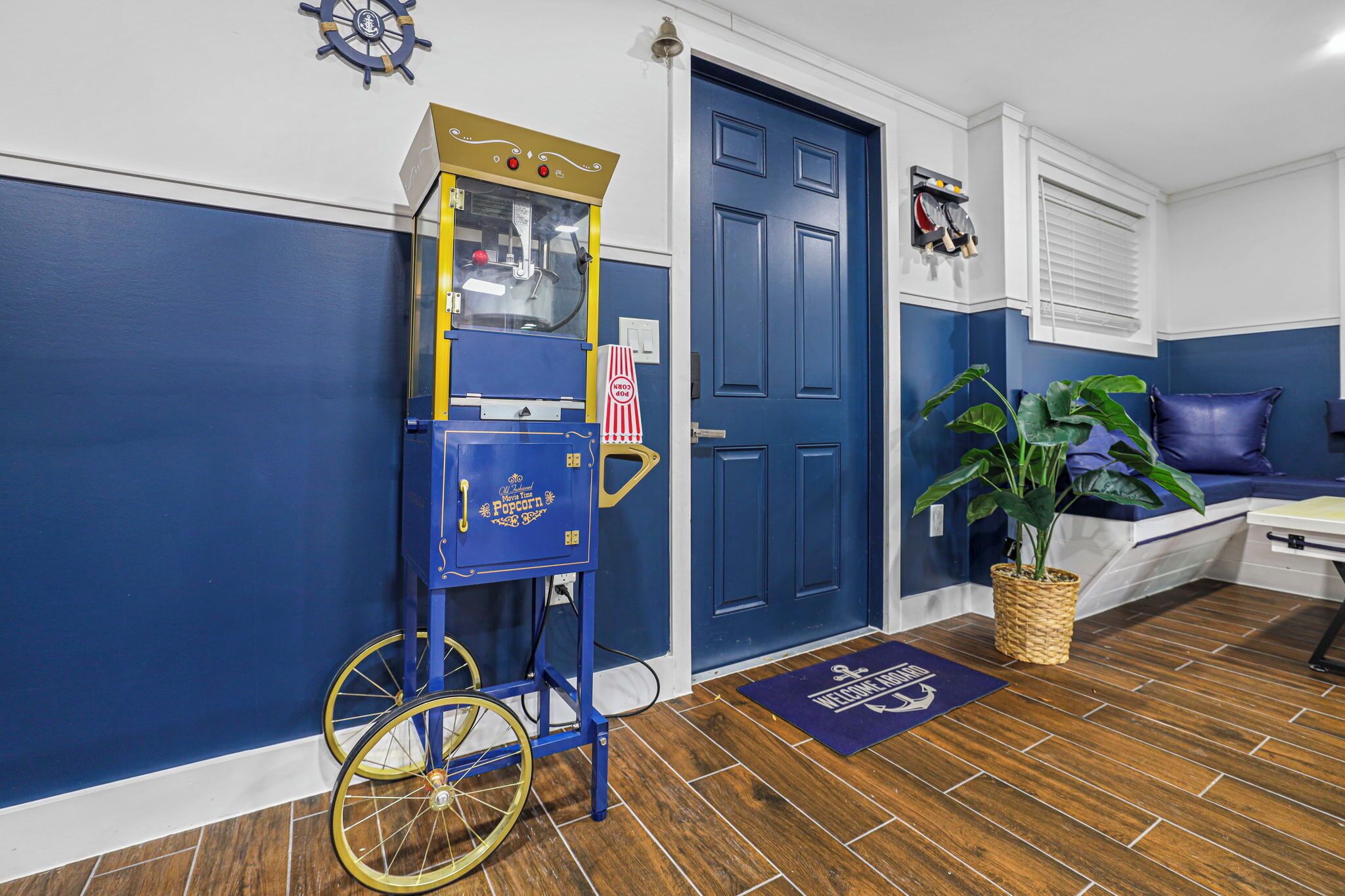 Una habitación con puerta azul, un carrito de palomitas, una planta y una decoración en tonos azul y blanco.