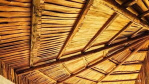 Ein rustikaler Raum mit einer hohen Holzbalkendecke, zwei Betten mit passenden Kopfteilen und einem großen Fenster mit Vorhängen.