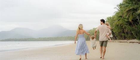 A family walking on a beach with palm trees and mountains in the background.