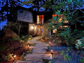 A modern house with a stone pathway leading to the entrance, surrounded by greenery.