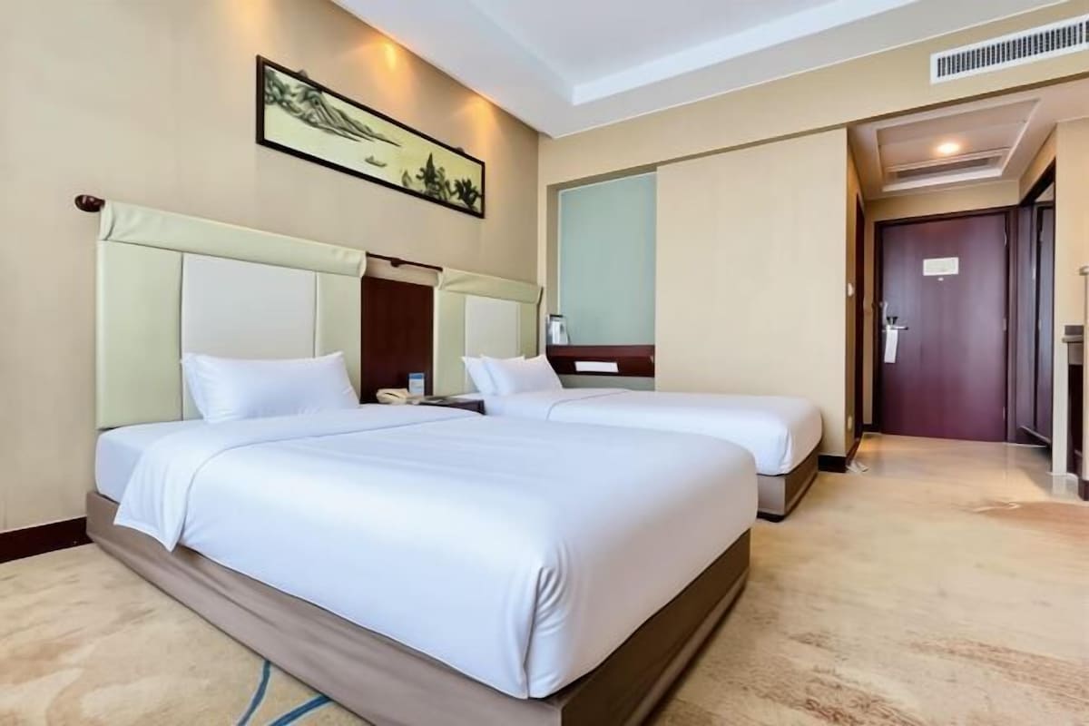 A hotel room with two beds, a large mirror, a painting on the wall, and a carpeted floor.