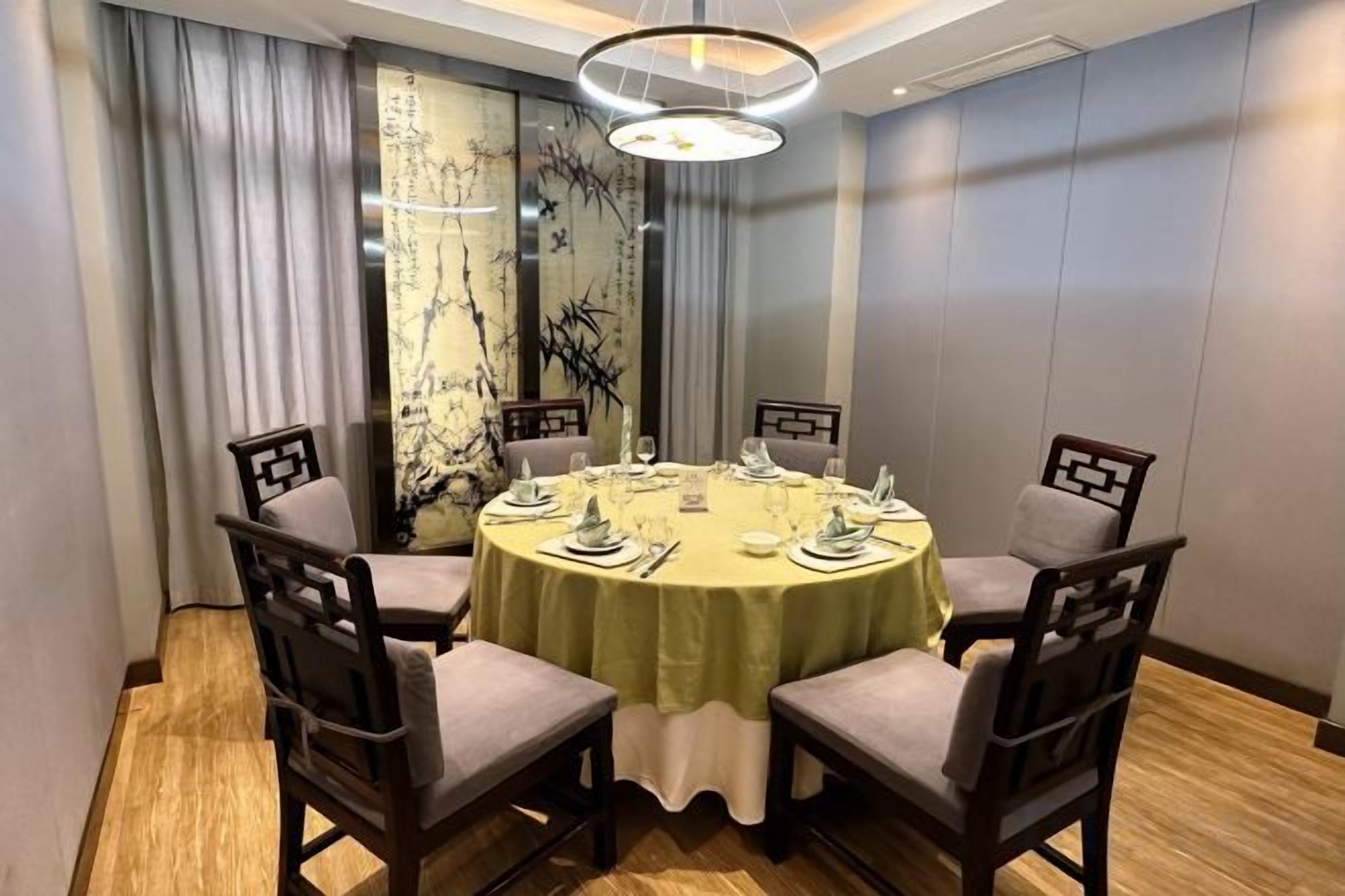 A round dining table with a green tablecloth, surrounded by four chairs with cushioned seats and dark wooden frames.