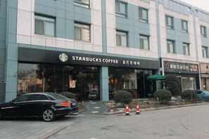 Una caffetteria Starbucks con un'auto parcheggiata davanti e un edificio con un cartello in lingua straniera.