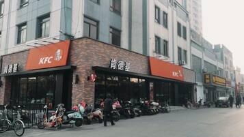 Restaurante KFC com mesas ao ar livre, bicicletas estacionadas na frente e um edifício com várias janelas ao fundo.