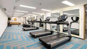 Egy fitneszközpont, amely futópadokkal és egyéb edzőeszközökkel van felszerelve, mintázott szőnyeggel rendelkezik, és egy folyosó vezet onnan egy pihenősarokhoz.