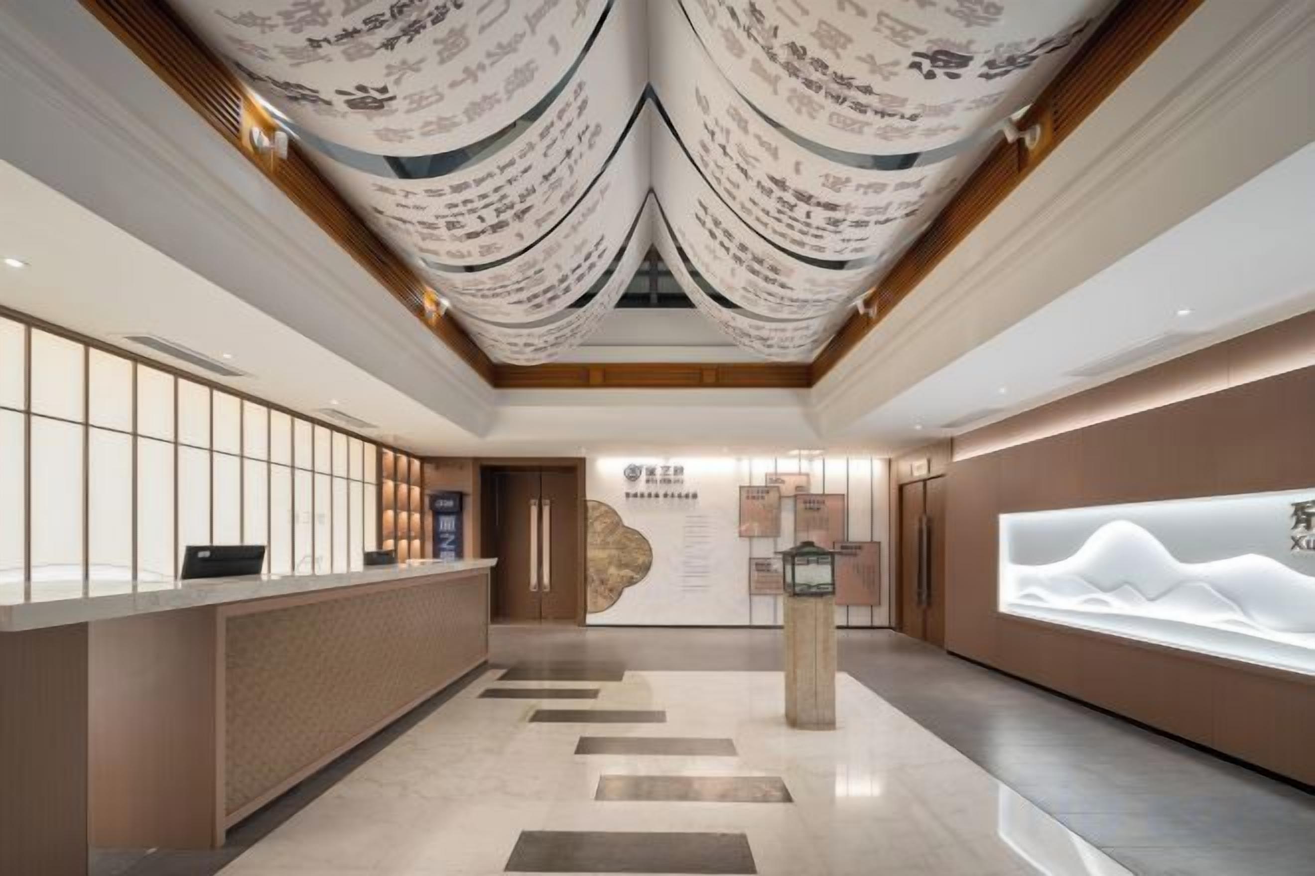 A hotel reception area with a reception desk, a wall-mounted information board, and a decorative ceiling.