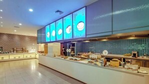 Egy modern étterem, ahol egy hosszú pult, kék csempékkel borított fal és megvilágított menütáblák találhatók.