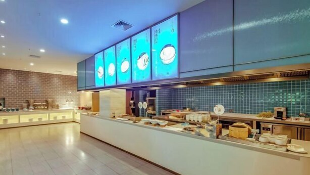A modern restaurant with a long counter, blue-tiled backsplash, and illuminated menu boards. - SCHOLARS HOTEL·SELECT Collection Hotel (Suzhou Shilu Sanxiang Road Subway Station) (Suzhou)