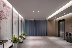 Un vestíbulo de hotel con piso alfombrado, una cortina azul y una recepción con plantas en macetas.