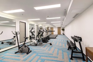 Gimnasio de hotel con equipo de ejercicio, espejos y una alfombra estampada.