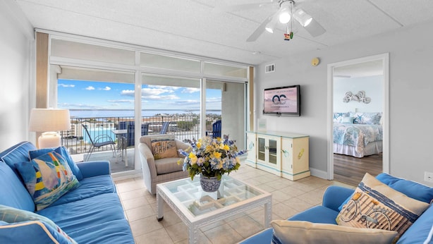 Ein geräumiger Wohnbereich mit Balkon, Deckenventilator, Fernseher und Meerblick.