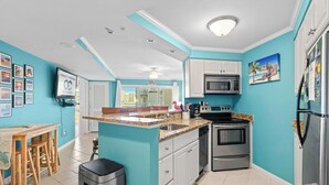 Een keuken met turquoise wanden, witte kasten, een granieten aanrechtblad, roestvrijstalen apparatuur en een plafondventilator.