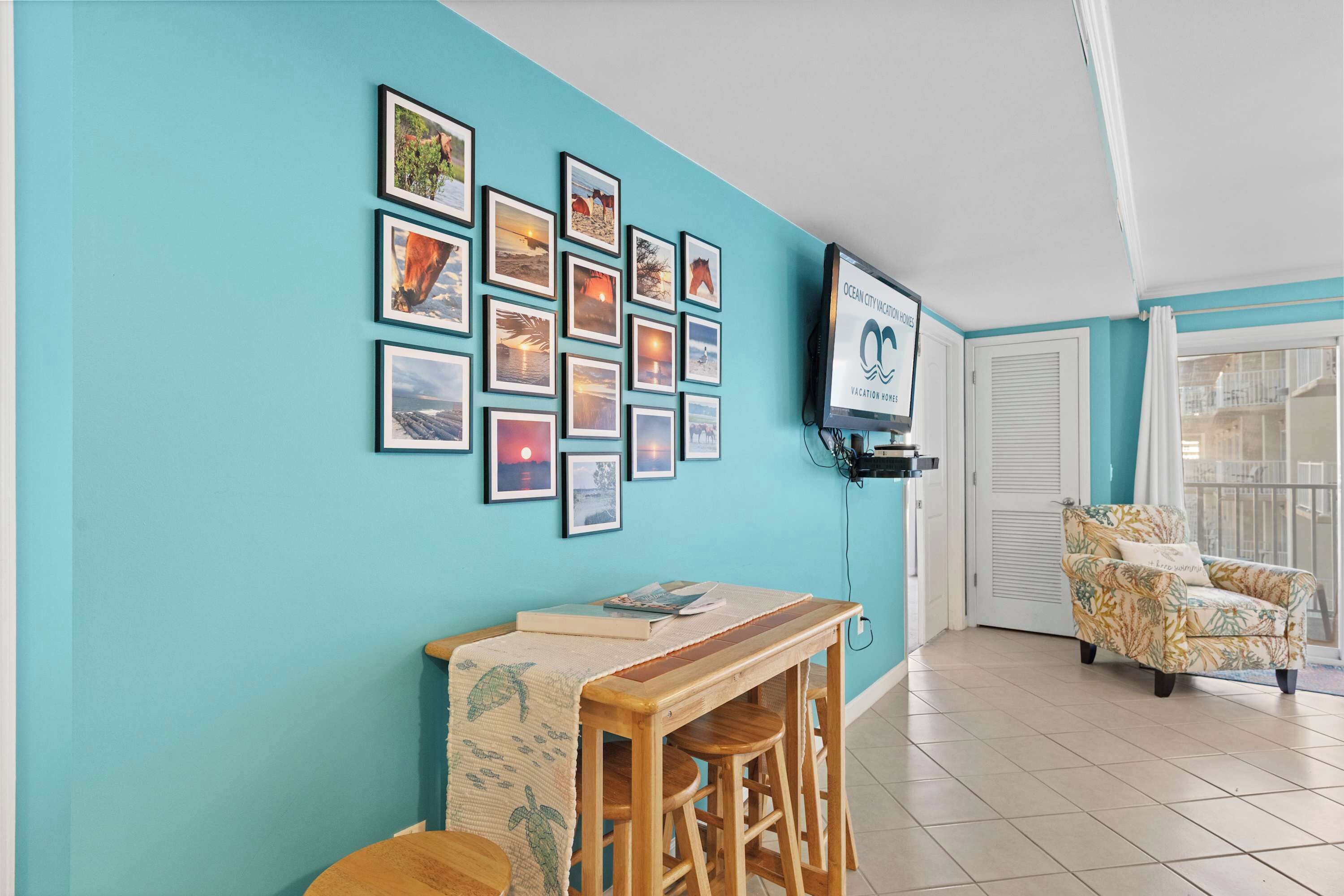 Een kamer met teal muren, een houten tafel met een boek, een gestreept fauteuil en een tv aan de muur met een logo.