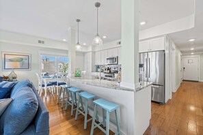 A modern kitchen with white cabinets, stainless steel appliances, and a central island with bar stools. - Bayview Grand 102 (Ocean City)