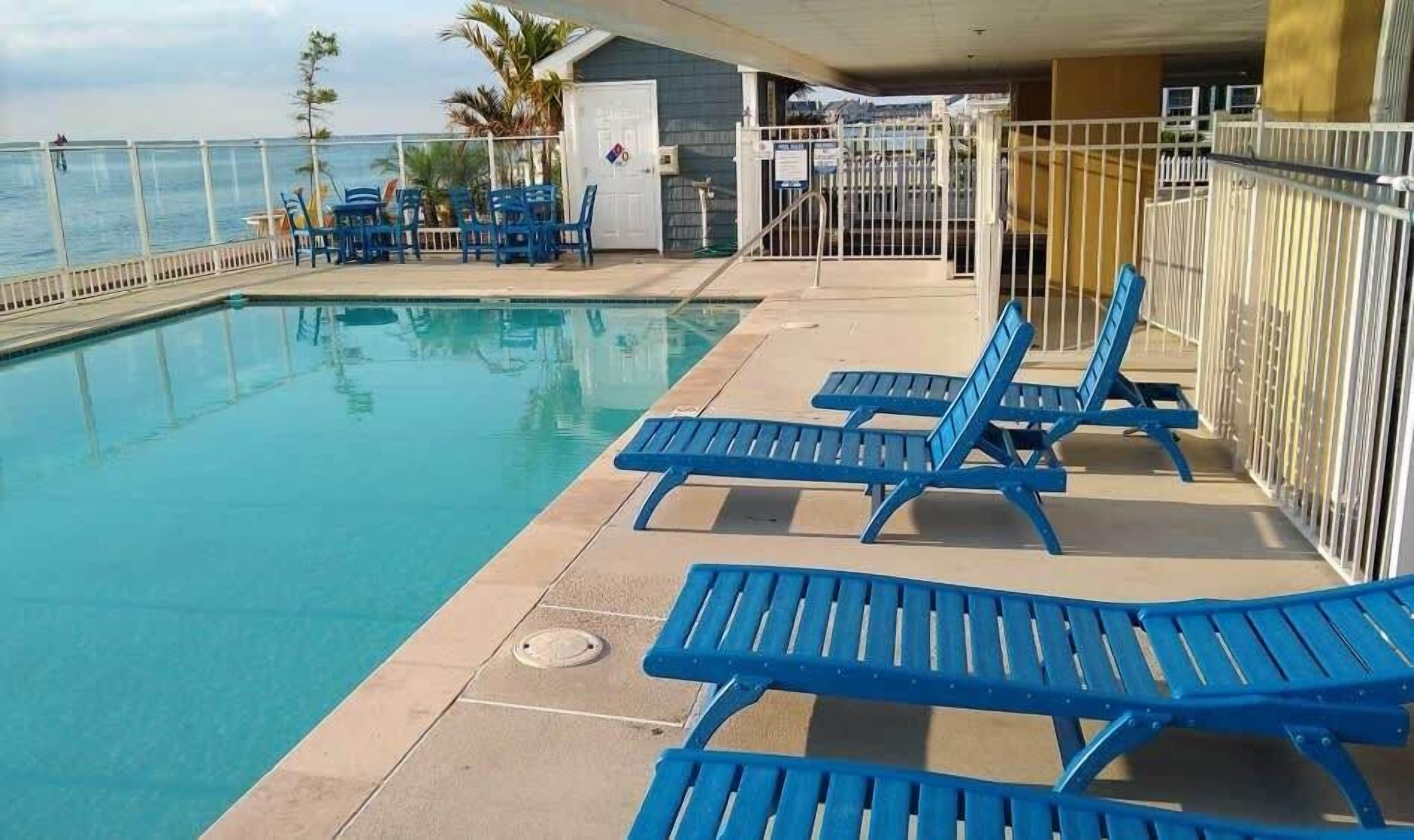 Zona de piscina con sillas reclinables azules y vista al mar.