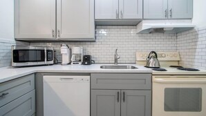 Una cocina moderna con armarios blancos, microondas, cafetera, hervidor y lavavajillas.