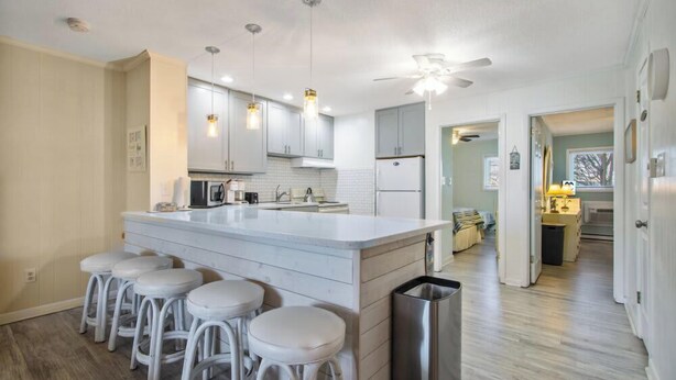Una cocina moderna con armarios blancos, una isla central con taburetes y un ventilador de techo.