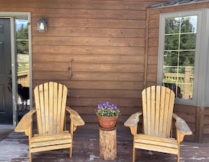 Two wooden Adirondack chairs on a wooden deck with a potted plant between them. - Charming 3-bedroom house in Seeley Lake for a relaxing stay (Seeley Lake)