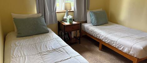 A room with two single beds, a bedside table with a lamp, and a window with curtains.