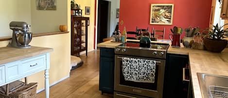 Una cocina con horno integrado, una batidora y un comedor con sillas y mesa.