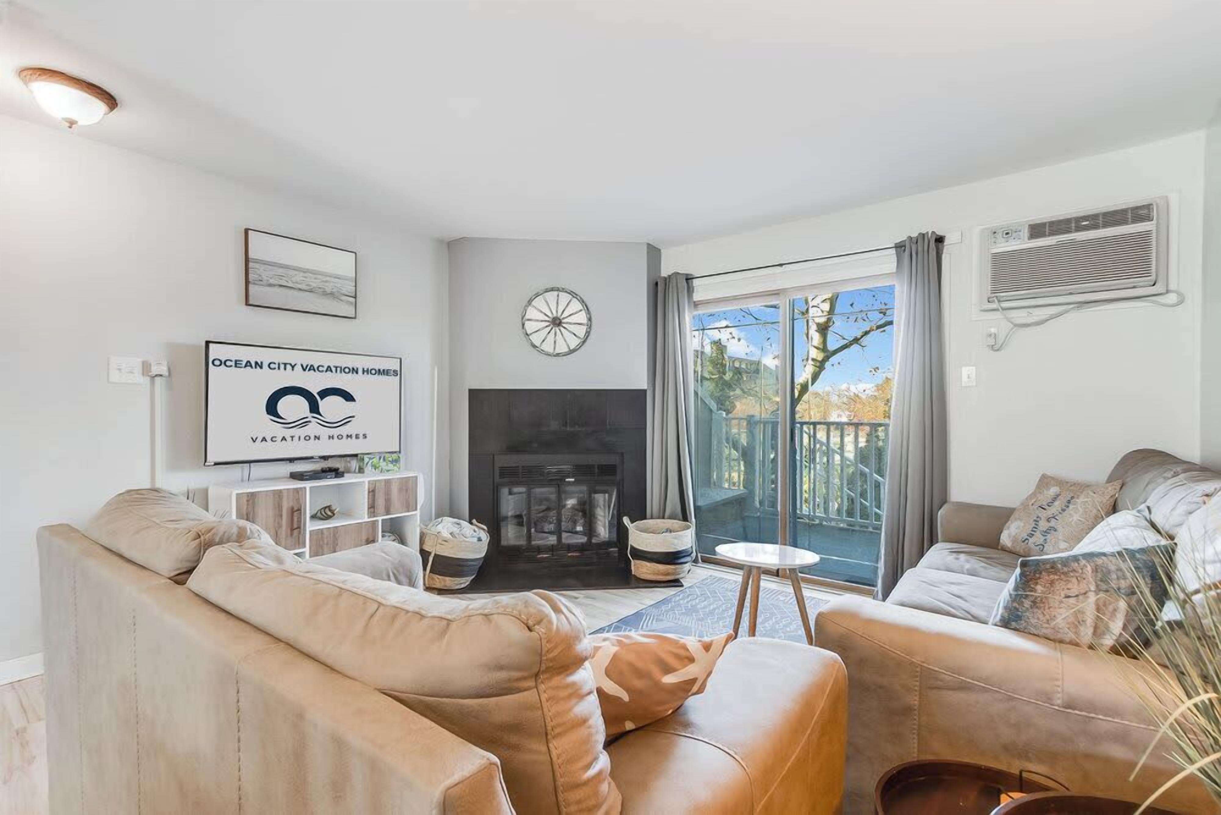A living room with two sofas, a fireplace, a television, and a large window with a view of trees.