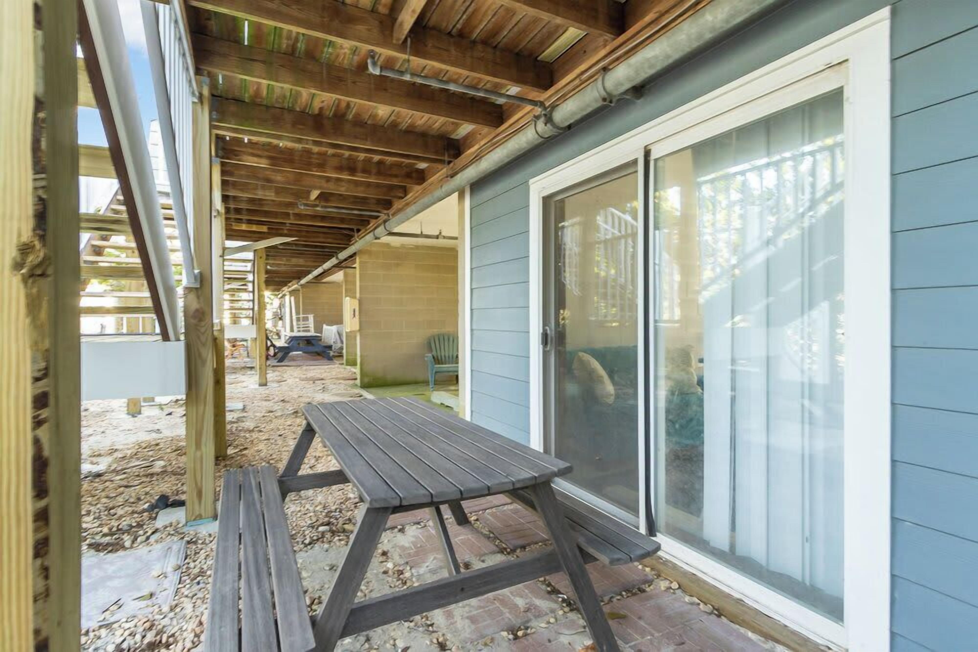 En overdækket terrasse med et træbord og stole, en skydedør og udsigt til baghaven.