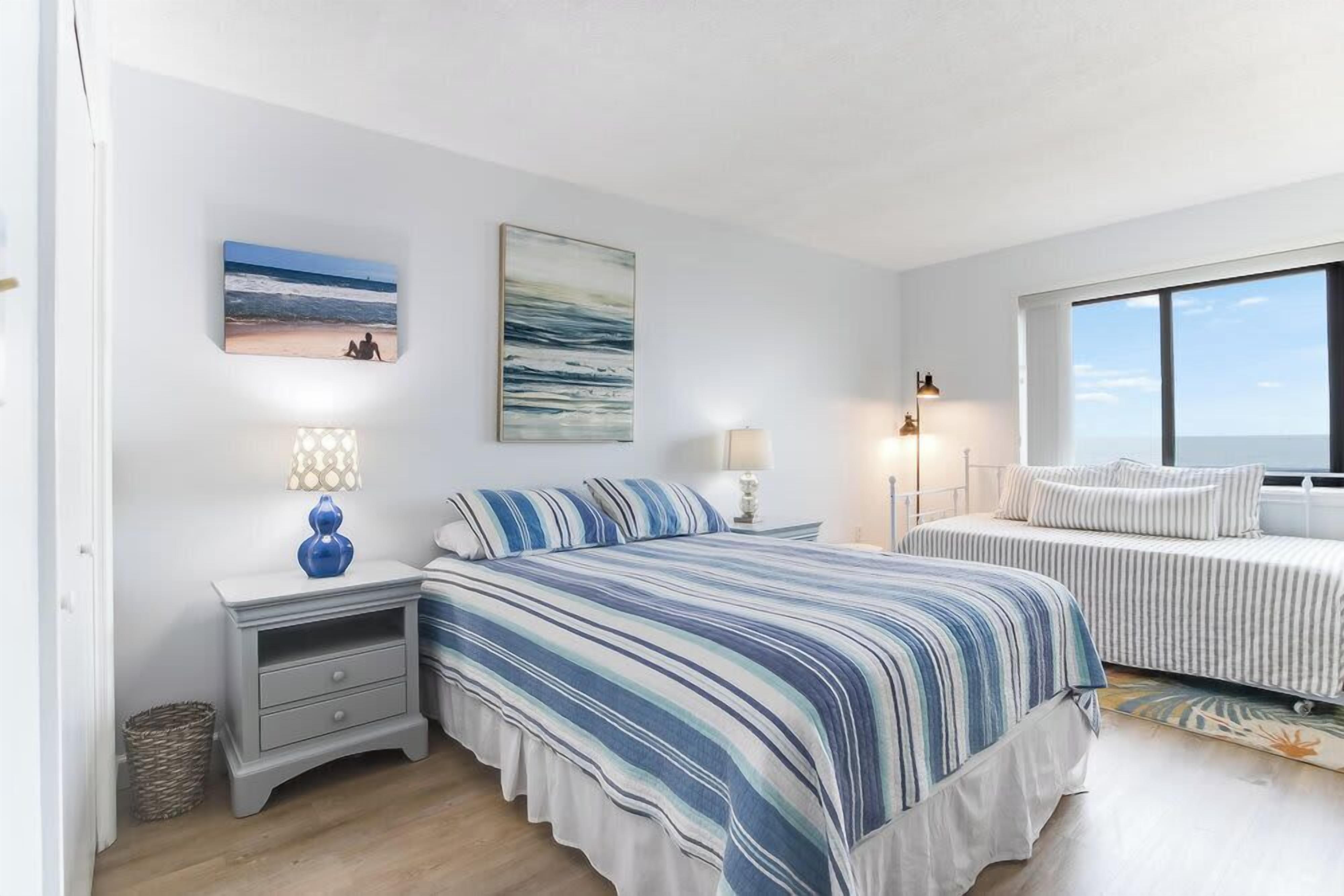 A bedroom with a large bed, a smaller bed, two bedside tables, and a view of the sea.