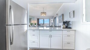 Eine moderne Küche mit weißen Schränken, einem Edelstahlkühlschrank und einer großen Kochinsel mit Kaffeemaschine.