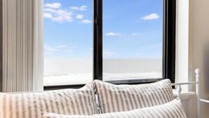 Ein Bett mit gestreiften Kissen und Blick auf den Strand durch große Fenster.