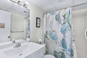Ein Badezimmer mit einem weißen Waschbecken, einem Spiegel und einem Duschvorhang mit Meeresmotiven.