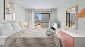 A hotel room with a bed, a desk, a lamp, a mirror, and a view of the city through the window. - Angelfish 207 (Ocean City)