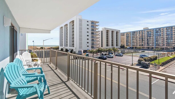 A balcony with two chairs, a view of a parking lot, and high-rise buildings in the background. - Angelfish 207 (Ocean City)