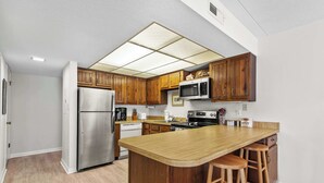 A kitchen with wooden cabinets, stainless steel appliances, and a central island with bar stools. - Angelfish 207 (Ocean City)