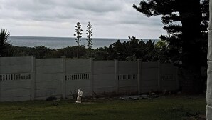 A fenced outdoor area with a grassy foreground and a view of the sea in the background.